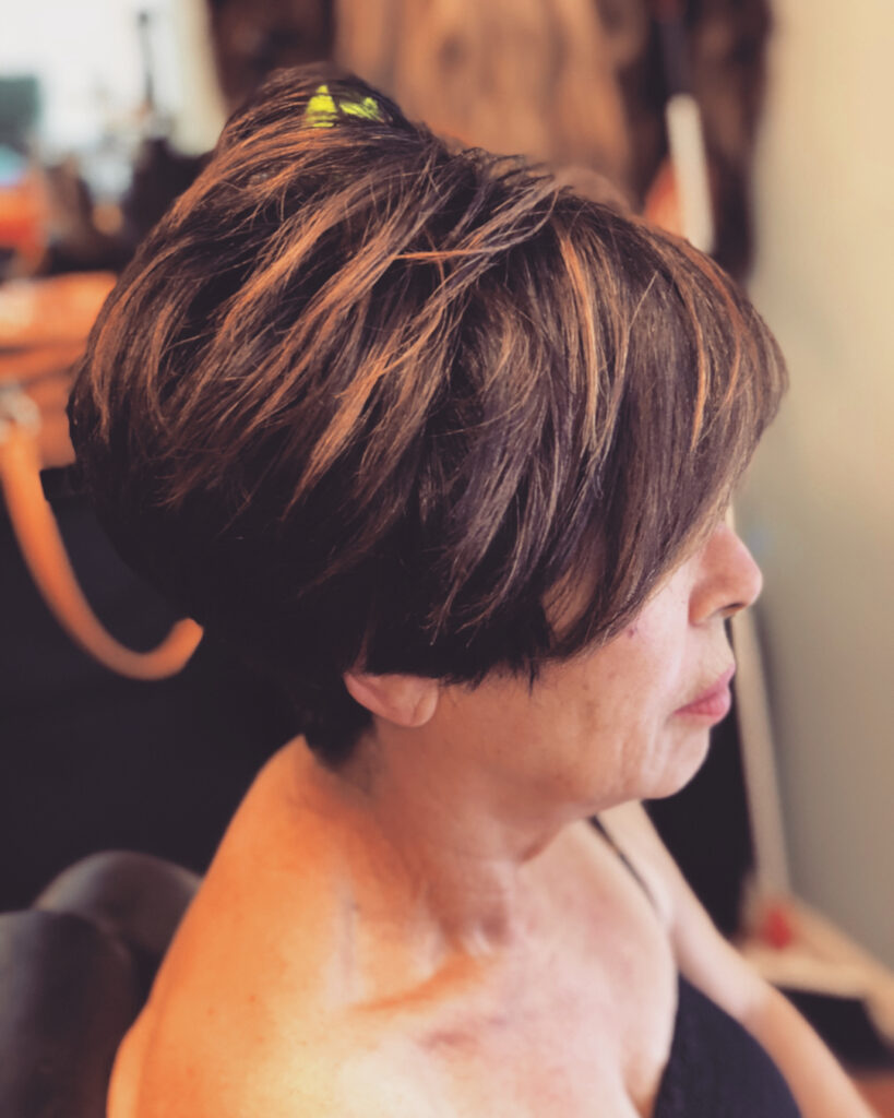 A woman in profile with a short brunette inverted bob featuring choppy layers and bright copper highlights.