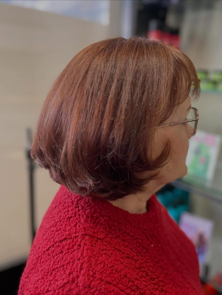 A woman with a shoulder-length auburn inverted bob hairstyle featuring soft layers and wispy front bangs.