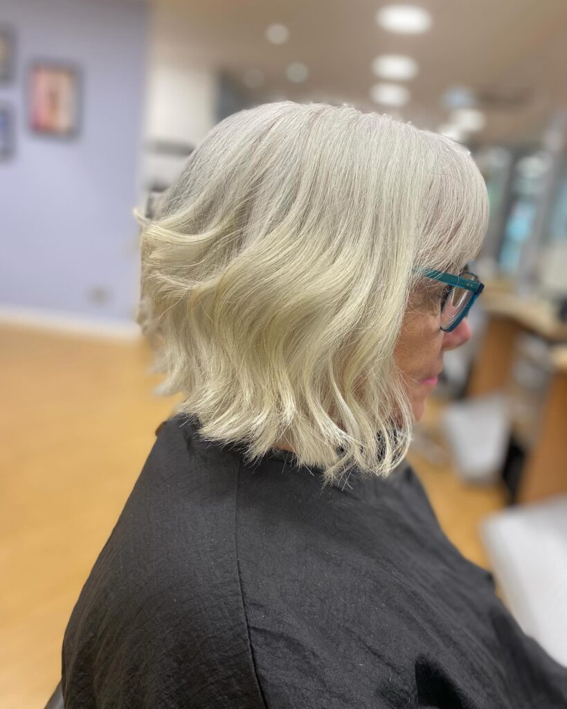 A woman from the side sporting a wavy white inverted bob with soft texture and a gentle angle.