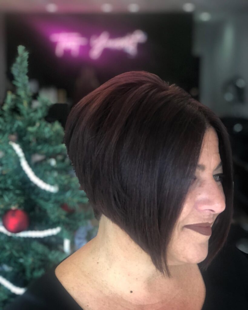 A woman in profile wearing a very sleek and steeply angled inverted bob in a dark plum purple shade.