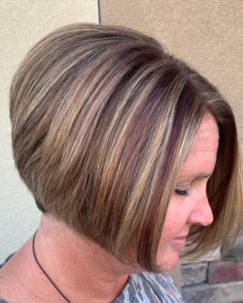 A woman with a brunette inverted bob hairstyle featuring bold blonde and reddish highlights and a sharp, angled cut.