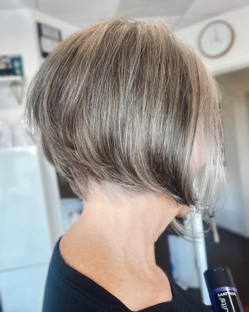 A side profile of a woman showing a natural grey and brown inverted bob with a visible undercut at the nape.