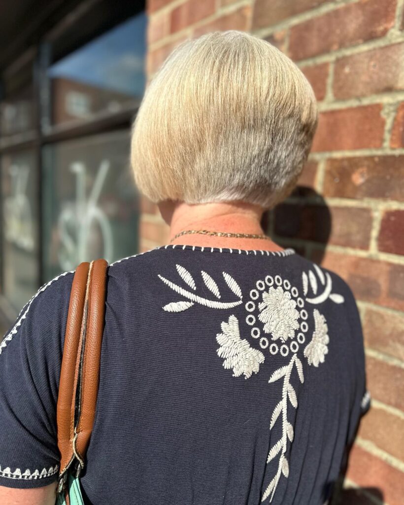 A back view of a woman with a straight, champagne blonde inverted bob featuring a rounded wedge shape at the nape.