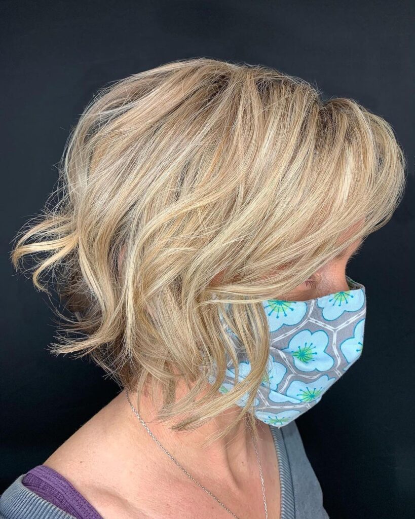 A woman with a wavy, champagne blonde inverted bob hairstyle featuring piecey layers and a stacked back.