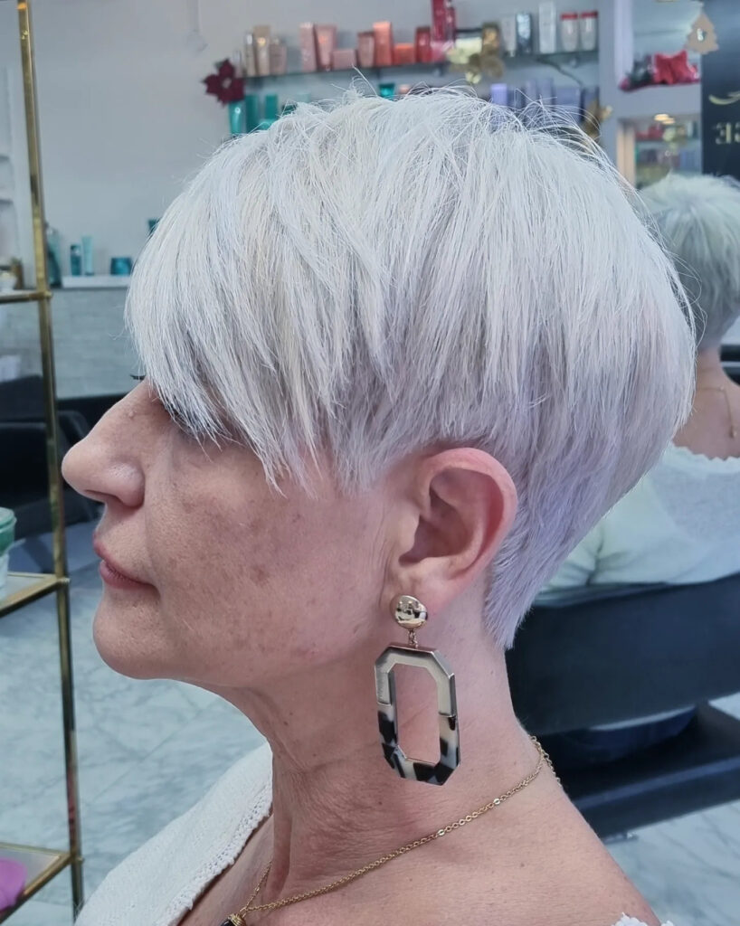 A woman with a short icy platinum pixie haircut featuring long textured layers on top and a tapered back.