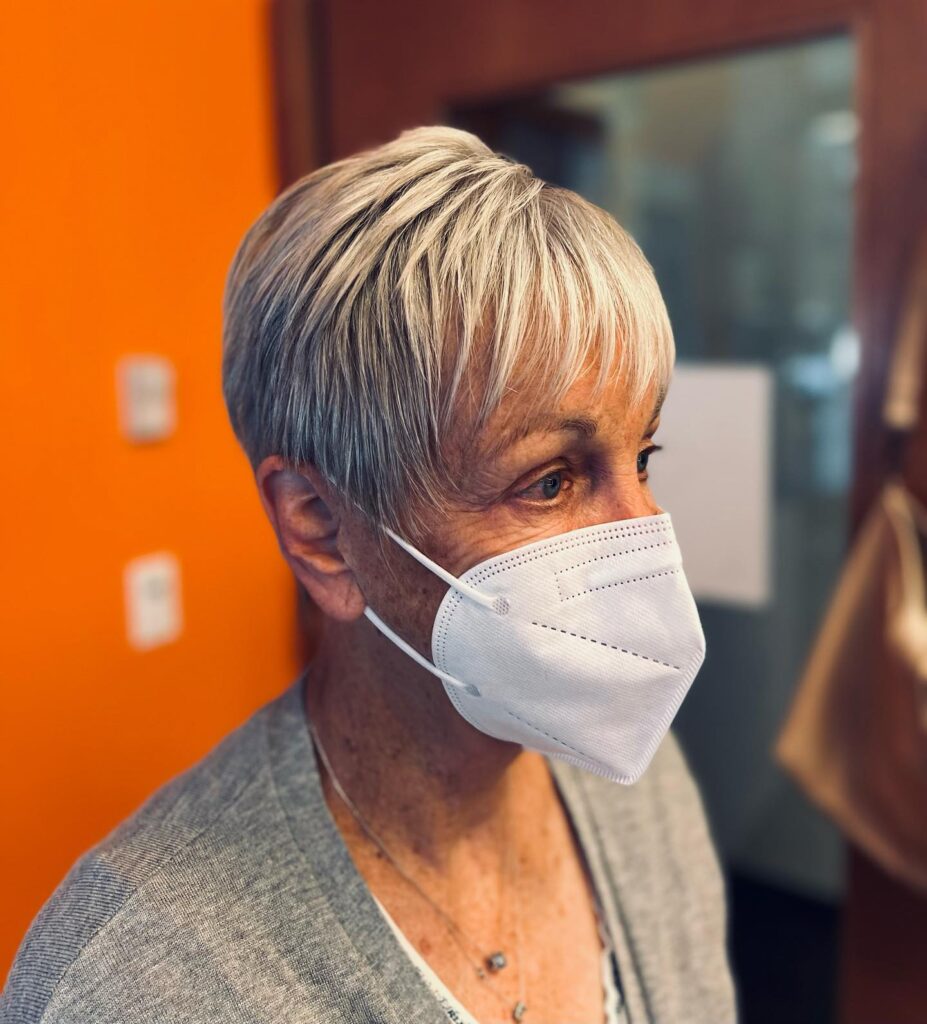 A woman with a sleek silver tapered pixie cut featuring fine texture and light wispy bangs.