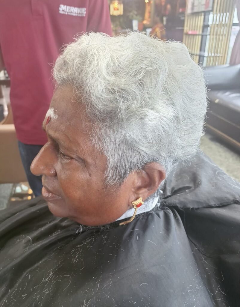 A woman with a voluminous silver pixie cut featuring natural curly texture and height at the crown.