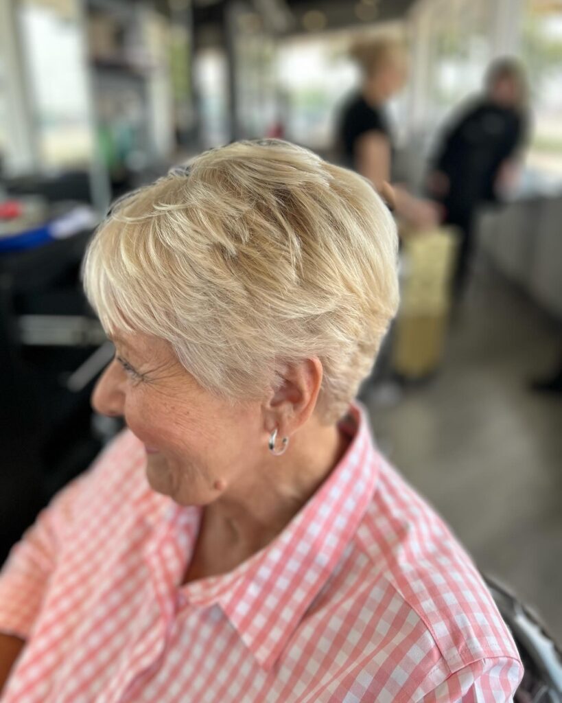 A woman with a feathered creamy blonde pixie haircut featuring soft layers and a side-swept fringe.