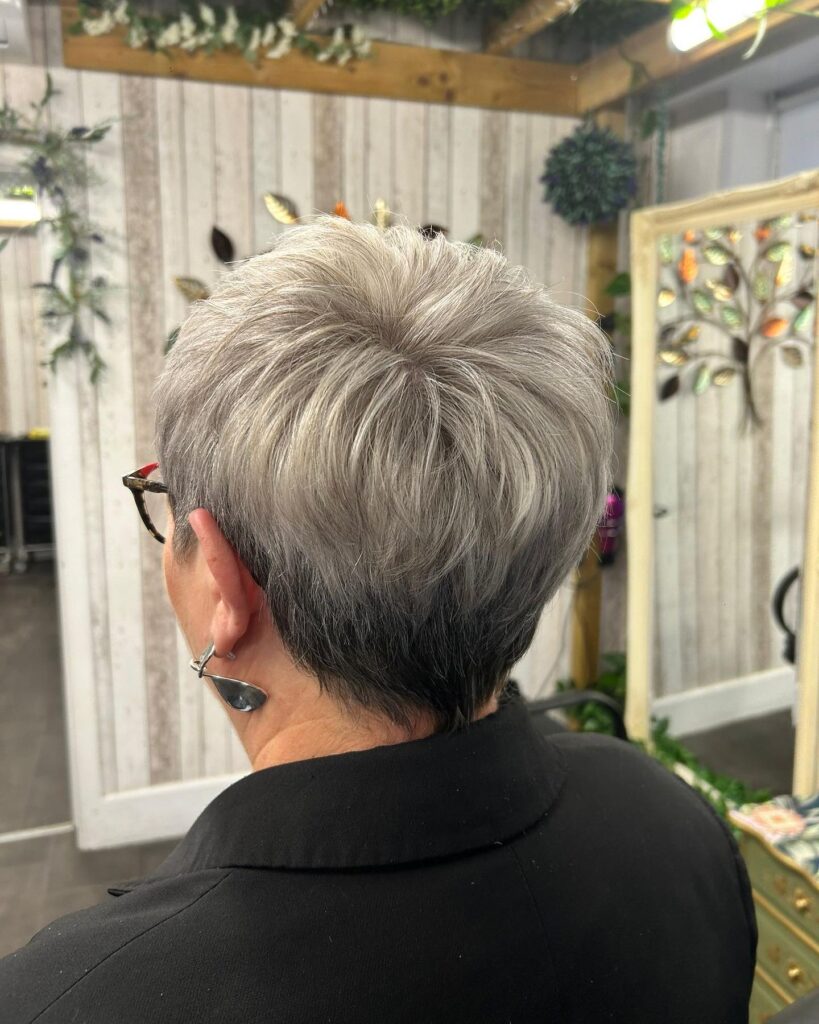 A rear view of a woman with a salt-and-pepper tapered pixie cut showing short dark hair at the nape and textured silver layers at the crown.