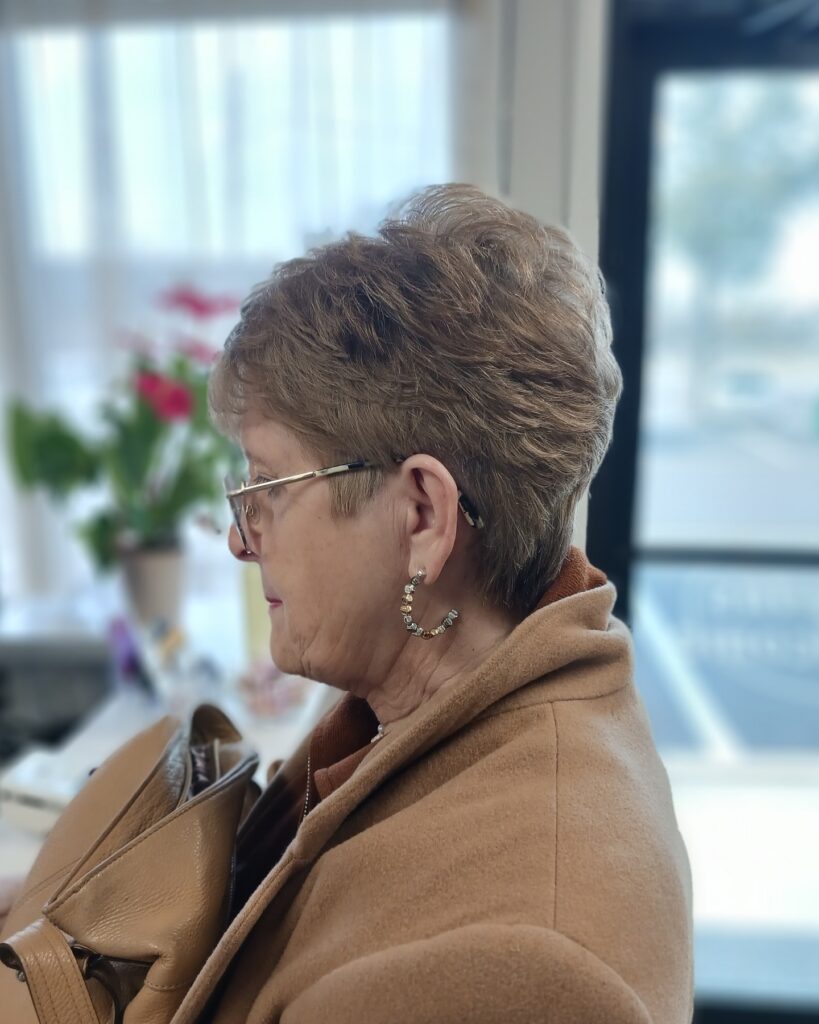 A side profile of a woman with an ash brown pixie cut featuring soft swept-back layers and volume at the crown.