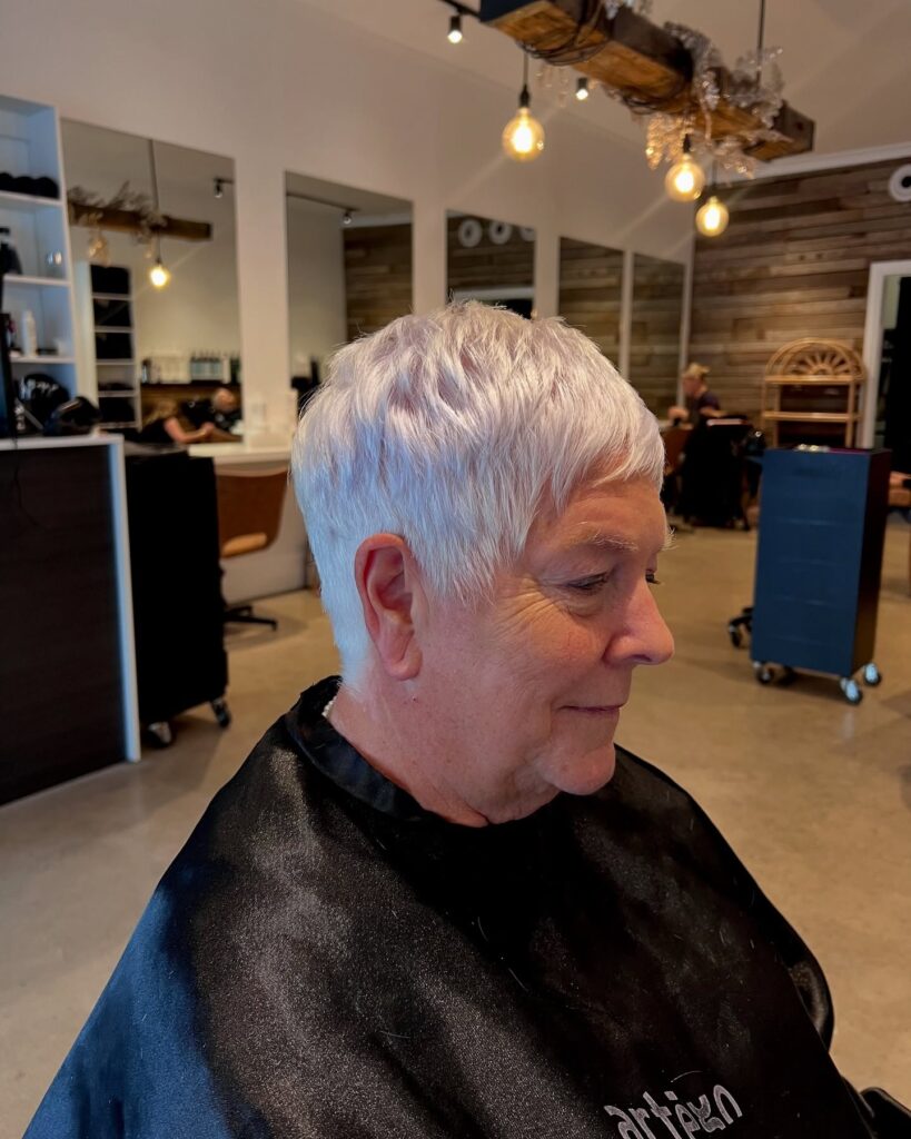 A woman in profile with a short textured pixie cut in a bright pearl white color featuring piecey layers.