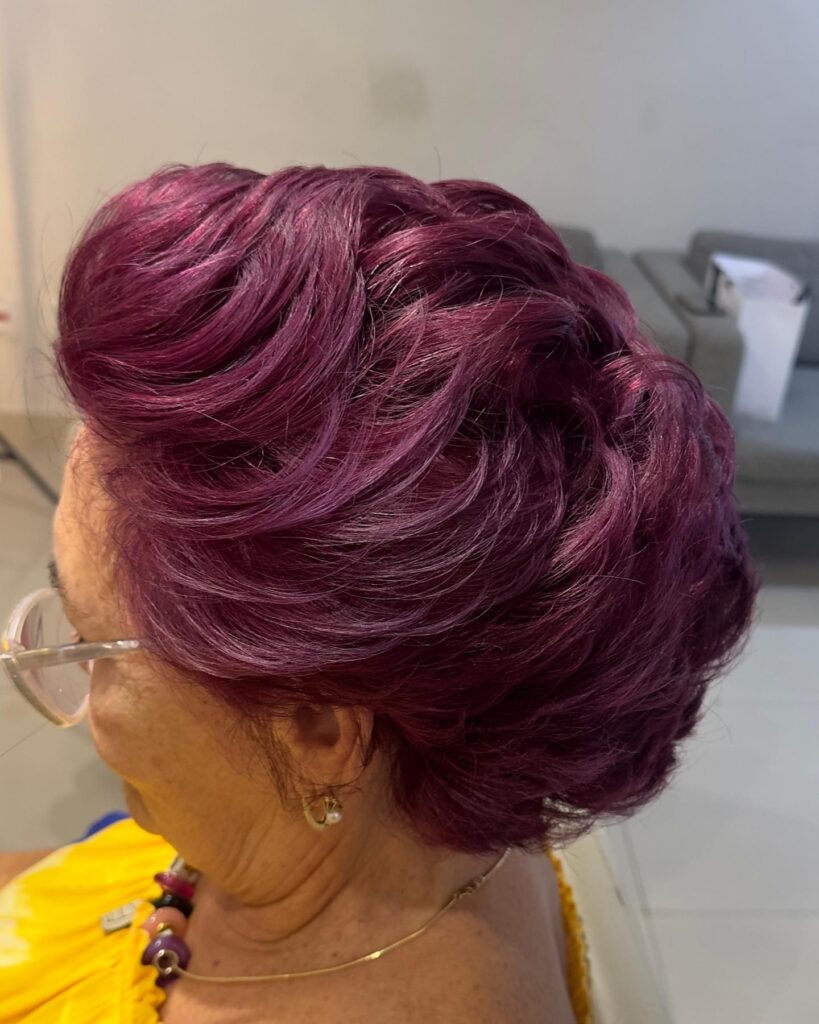 A woman showcasing a short layered bob in a vibrant, deep plum-purple color with voluminous swept-back waves.