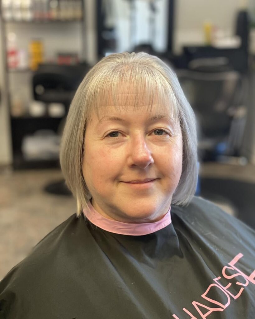A front view of a smiling woman over sixty with a sleek chin-length silver bob and light wispy bangs.