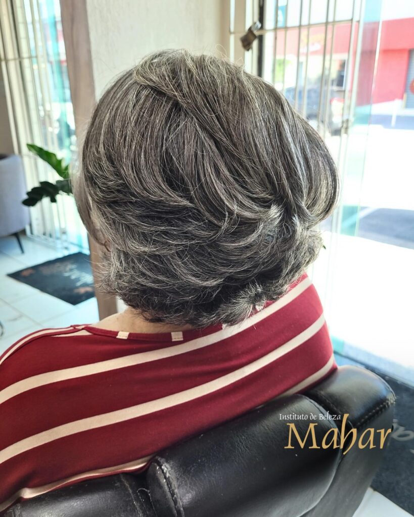 A back view of a woman with a short layered slate-grey bob featuring silver highlights and voluminous feathered styling.