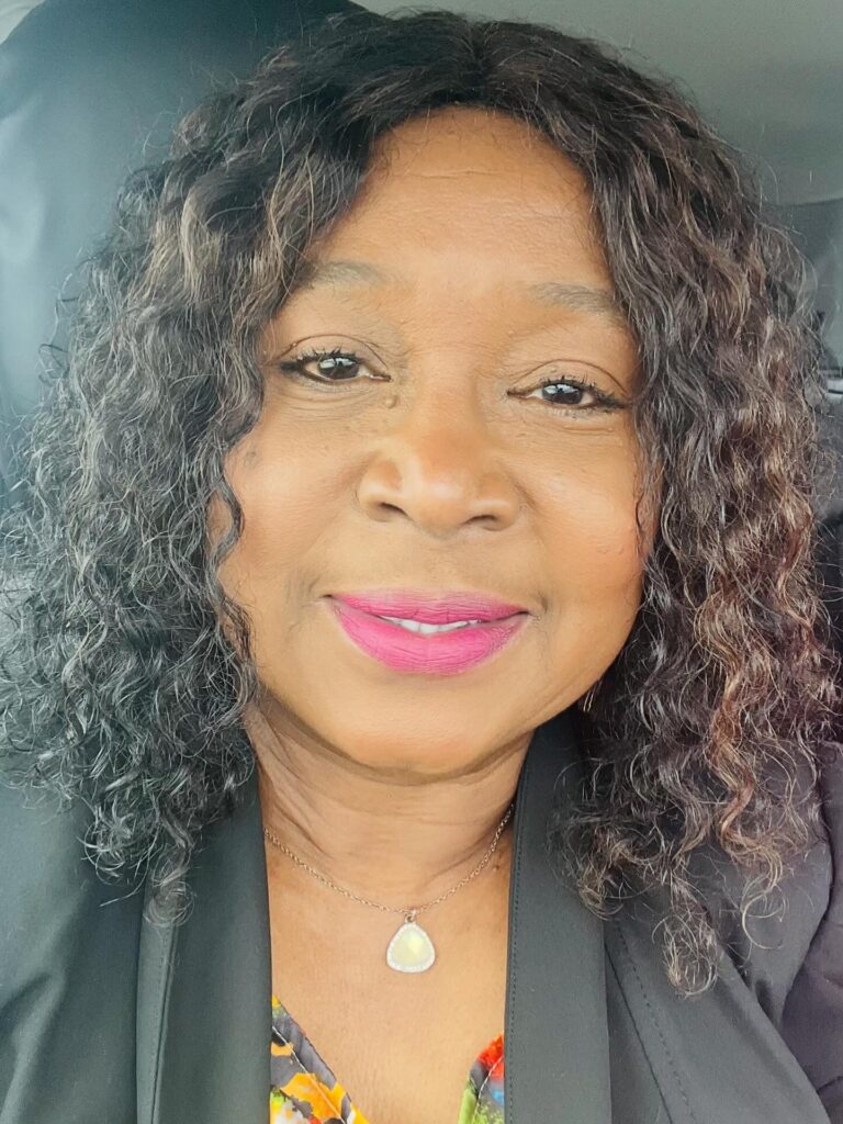 A woman over 60 with a round face wearing a shoulder-length curly hairstyle with dark hair and caramel highlights.