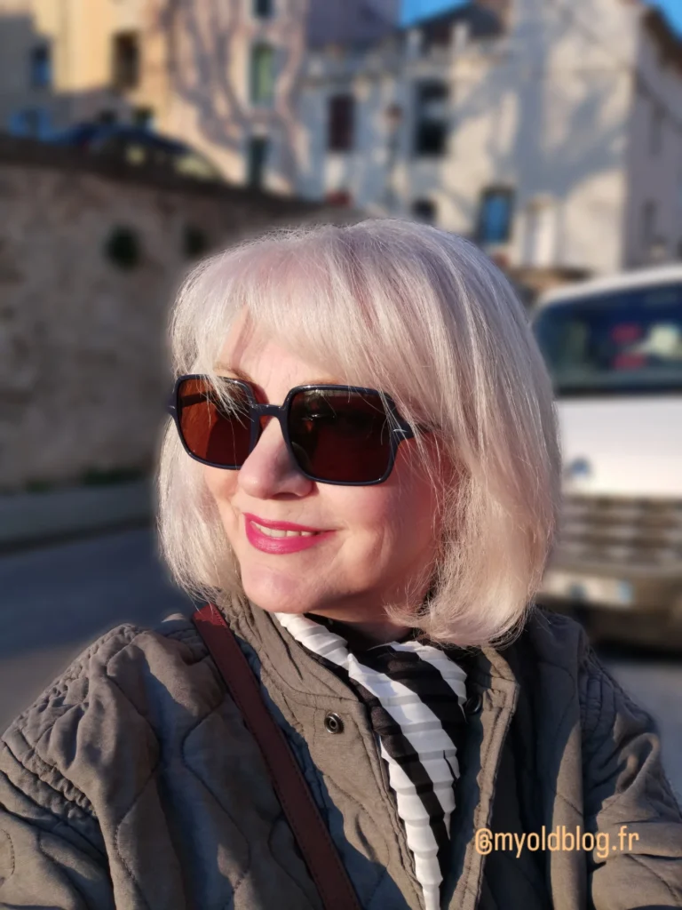 A woman over 60 with a round face wearing a sleek silver chin-length bob with a full straight fringe.