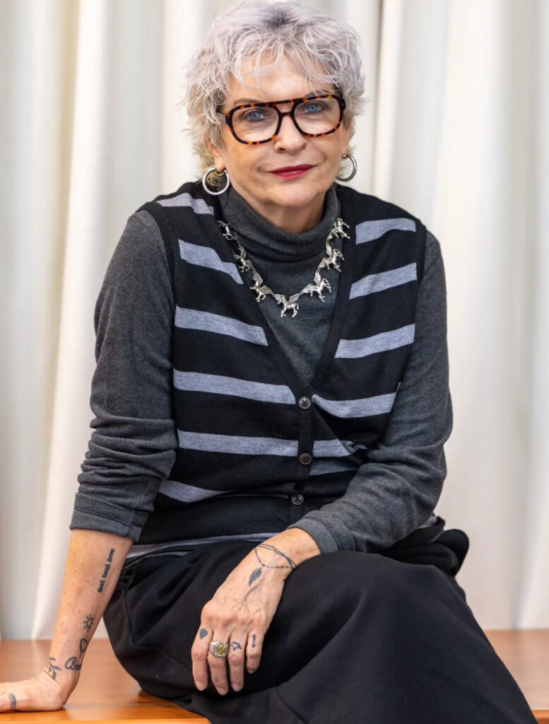 A woman over 60 with a round face wearing a short textured silver pixie cut with soft lavender tones and voluminous layers.