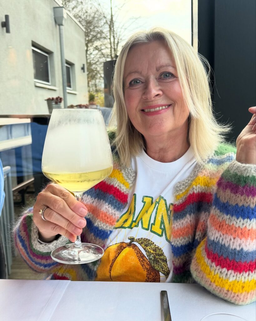 A woman over 60 with a round face wearing a shoulder-length pale blonde lob with soft, feathered face-framing layers.