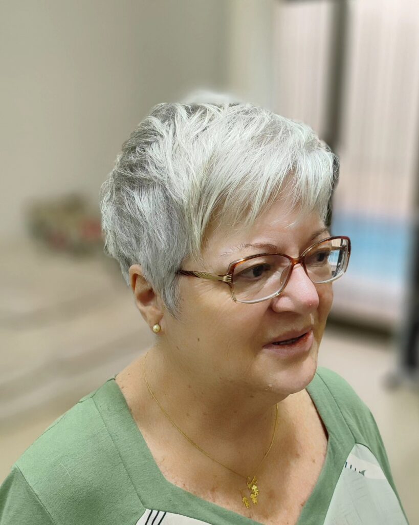 A woman with a textured silver and grey pixie cut featuring piecey bangs and soft layers.