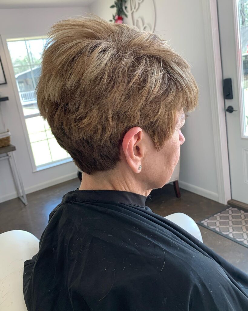 A woman with a piecey caramel pixie cut featuring feathered layers and a full fringe.