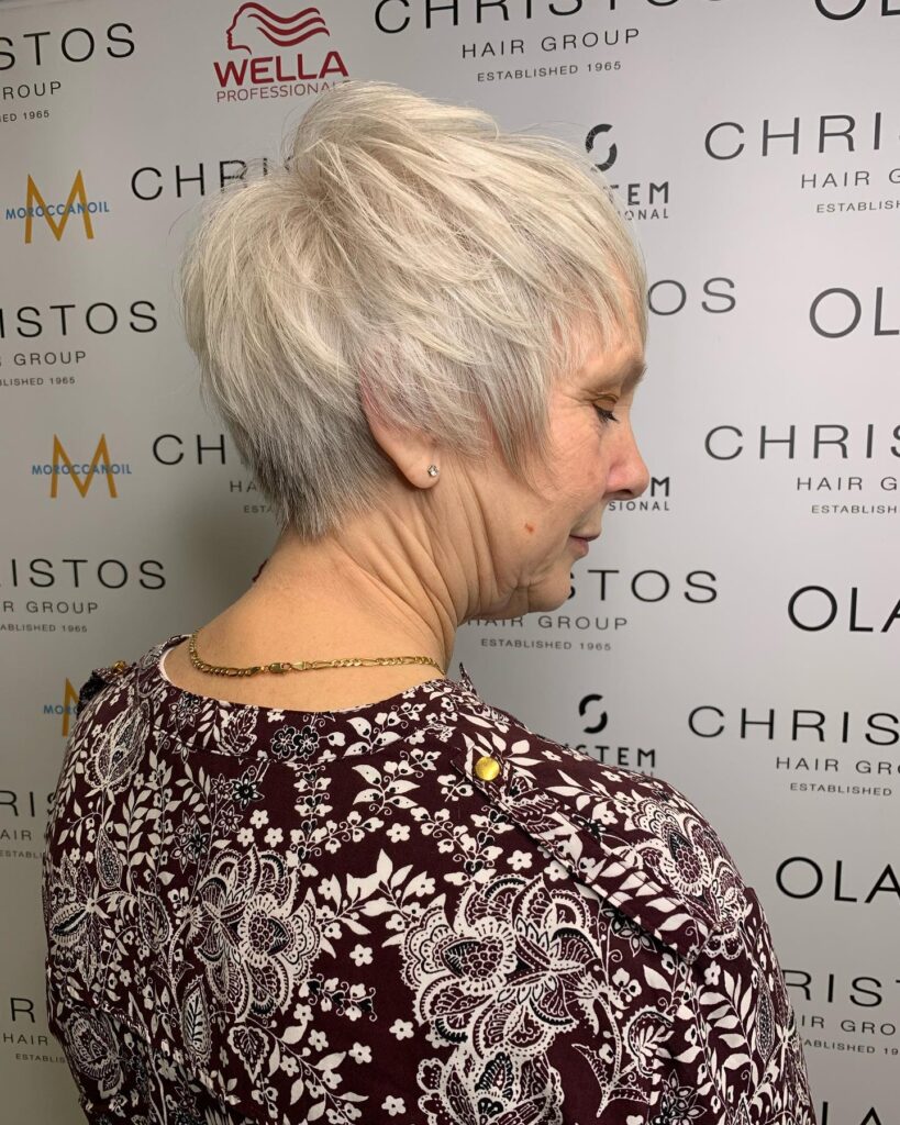 A woman with a feathered platinum blonde pixie haircut featuring long textured layers and a tapered back.