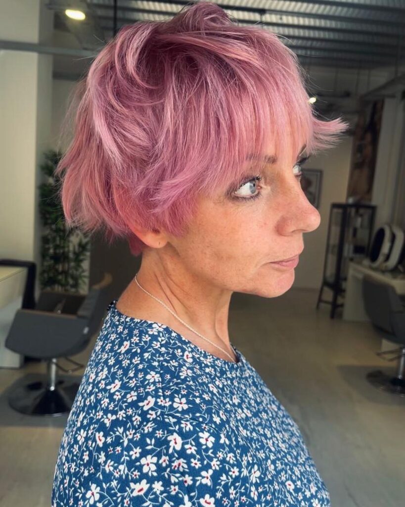 A woman with a shaggy rose pink pixie cut featuring wispy layers and feathery bangs.