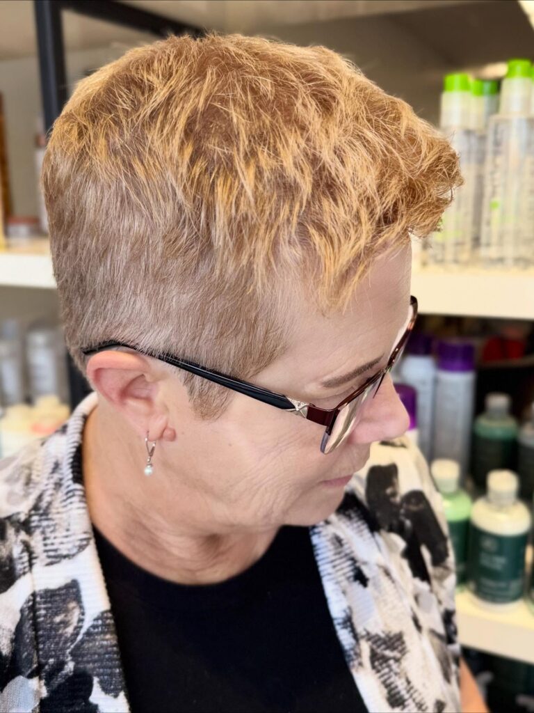 A woman in profile with a short strawberry-blonde pixie cut featuring a soft textured top and very short tapered sides.