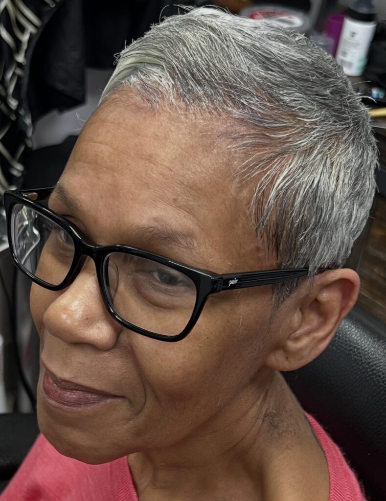 A woman wearing black glasses with a very short, sleek silver and charcoal pixie cut.