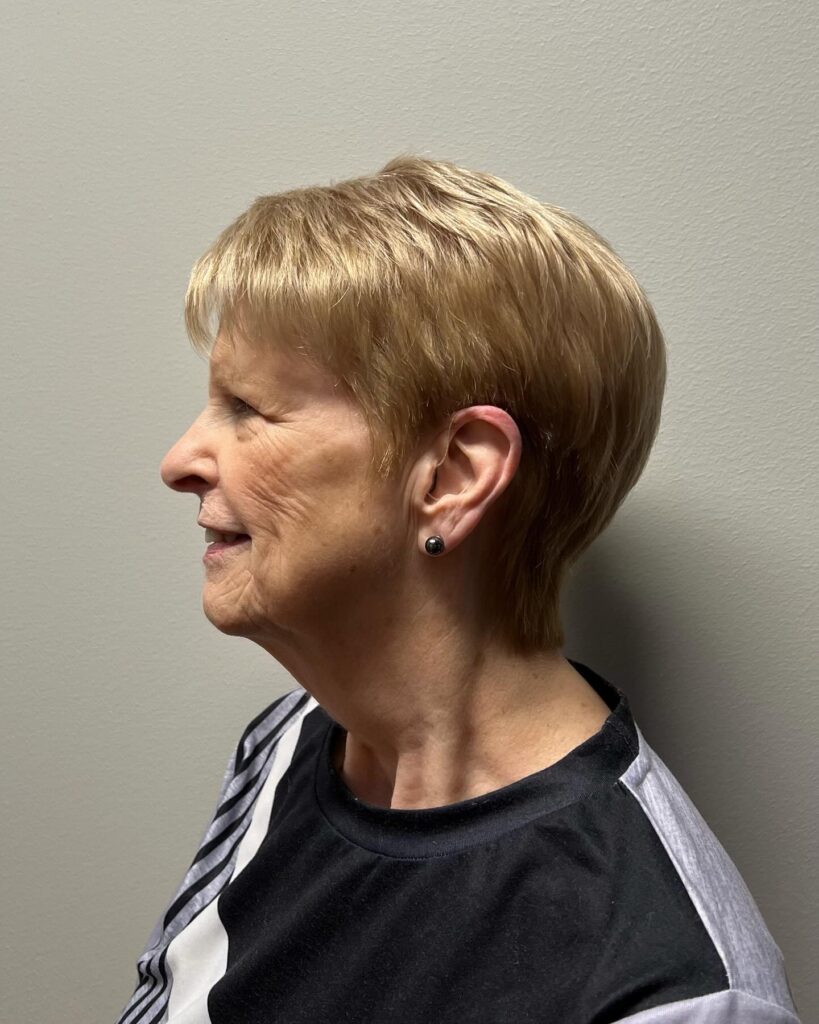 A woman in profile wearing a classic honey blonde pixie cut with a tapered back and short fringe.