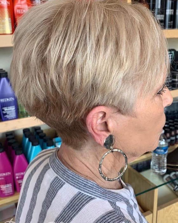 A woman in profile wearing a creamy vanilla blonde pixie cut with a tapered nape and soft crown layers.