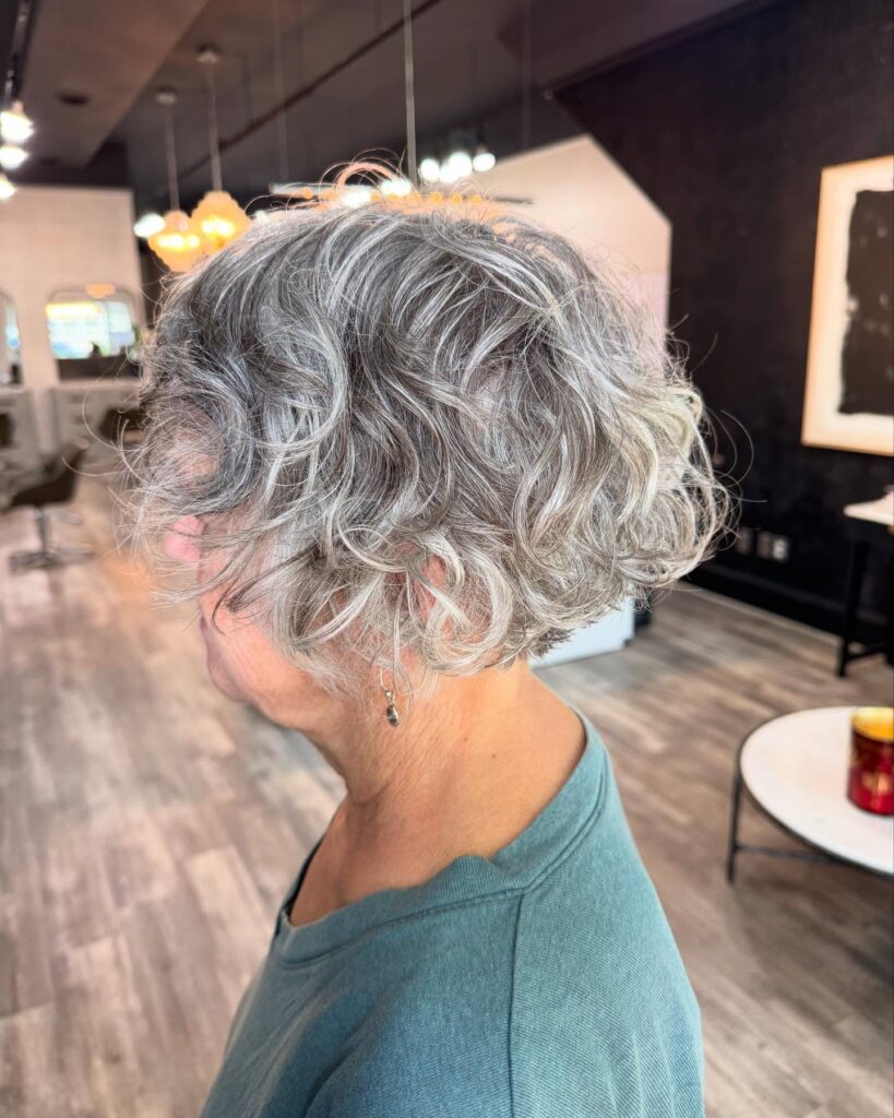 A woman over 60 with a wavy salt and pepper pixie cut featuring charcoal and silver highlights and voluminous layers.