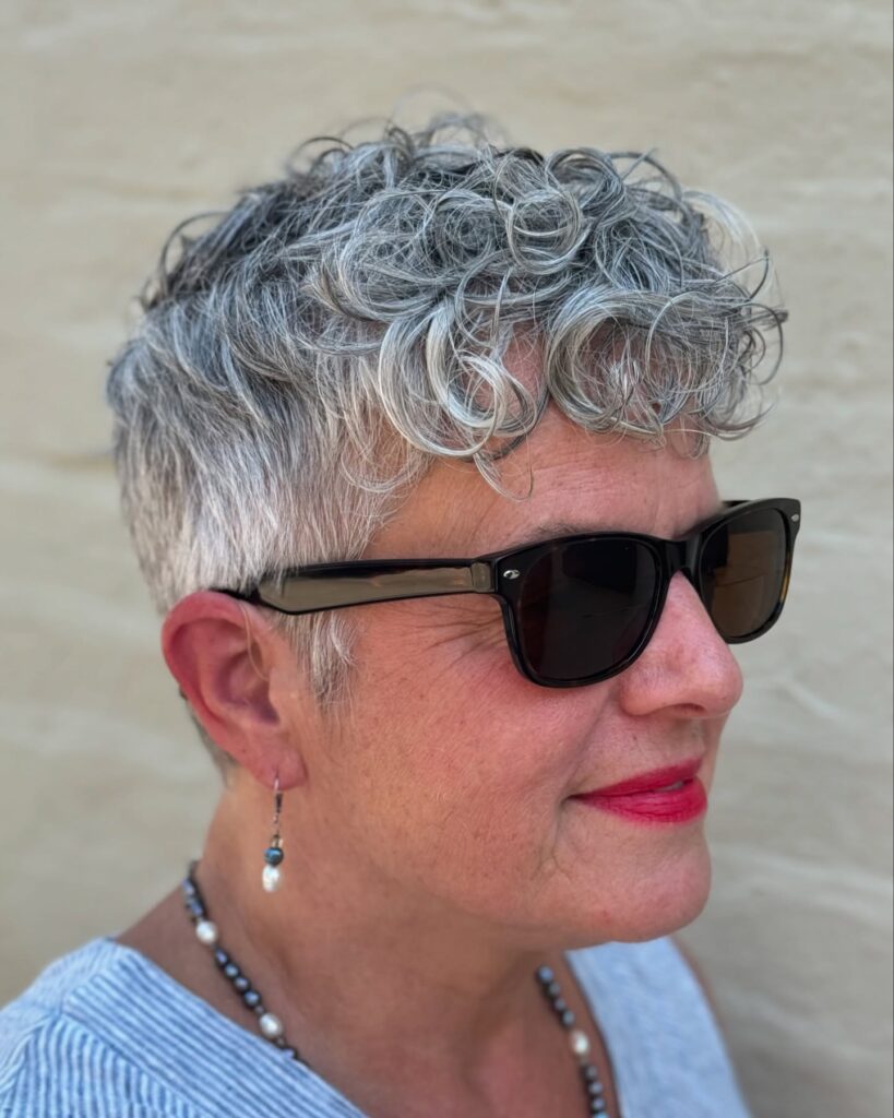 A side profile of a woman over 60 with a short, tapered pixie cut featuring silvery white curls and gray tones.