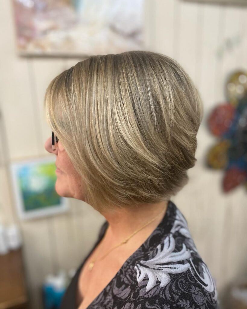 A woman in profile wearing an ash-blonde graduated bob with soft, wispy layers and light highlights.