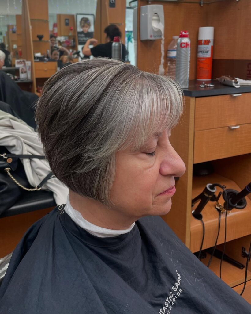 A woman over 60 with a short salt-and-pepper layered bob featuring a wispy fringe and silver highlights.