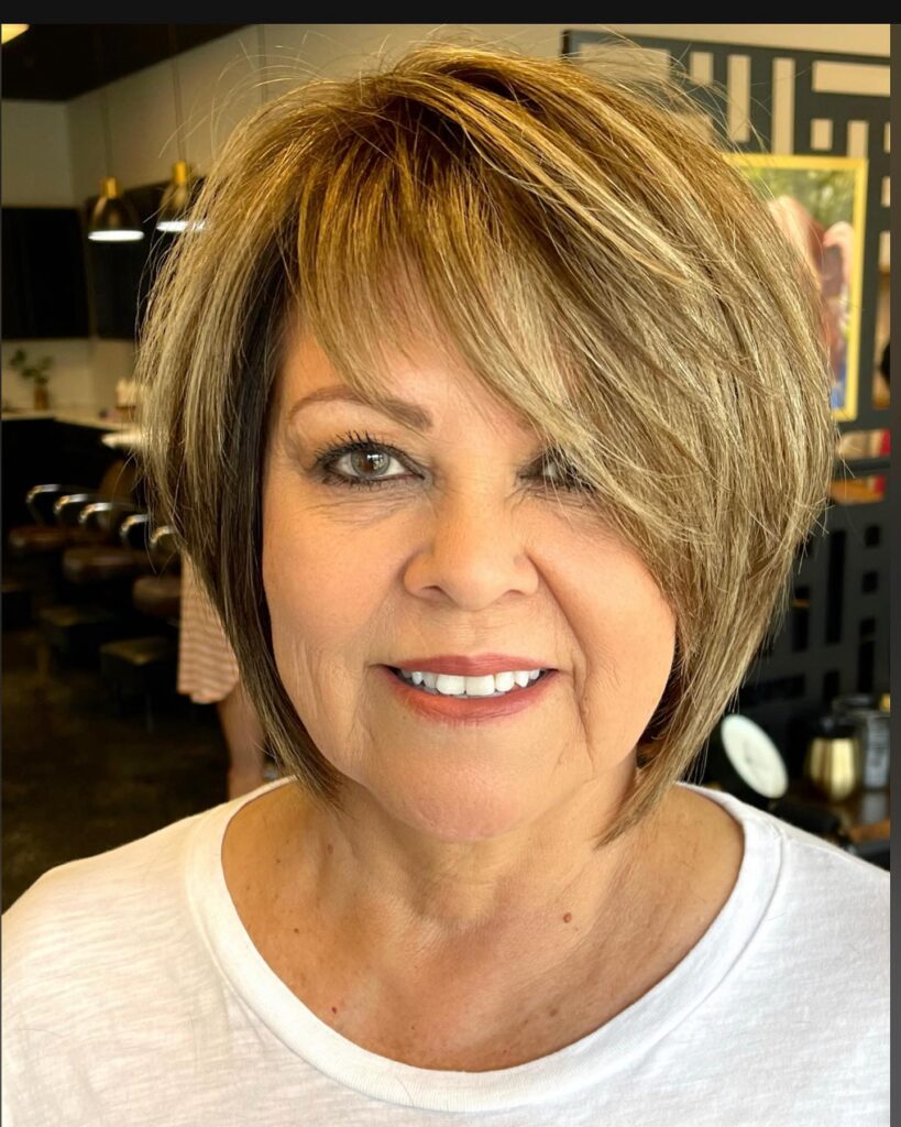 A woman over 60 with a textured bronde layered bob featuring caramel highlights and a deep side-swept fringe.