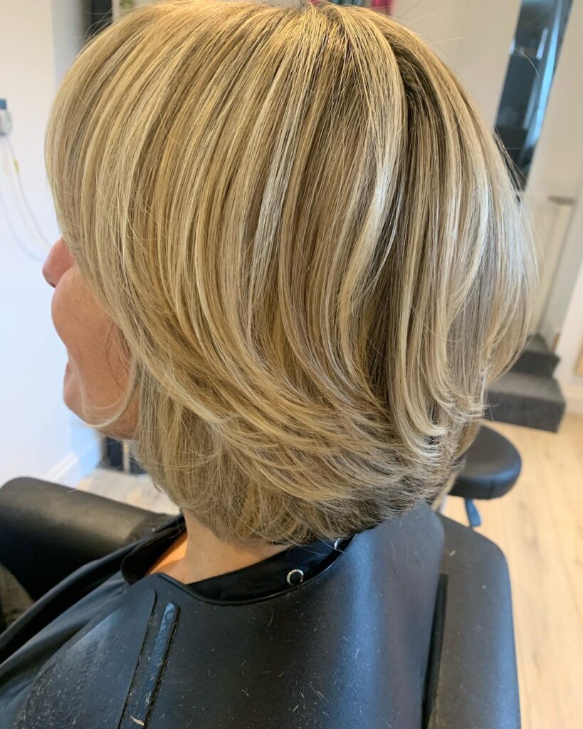 A woman with a sandy blonde layered bob showing curved ends and bright sun-kissed highlights.