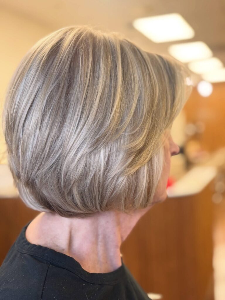 A woman with a champagne-silver layered bob featuring feathered tiers and multidimensional highlights.