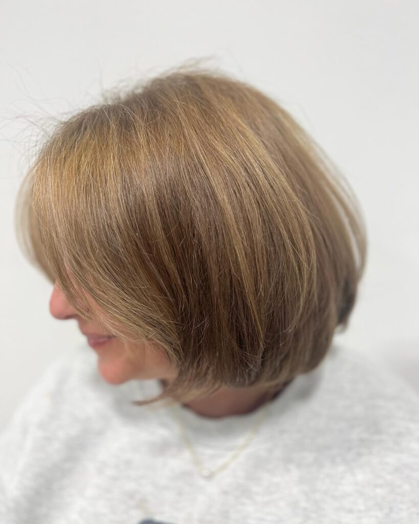 A woman with a chin-length caramel and honey blonde bob featuring soft internal layers and a smooth finish.
