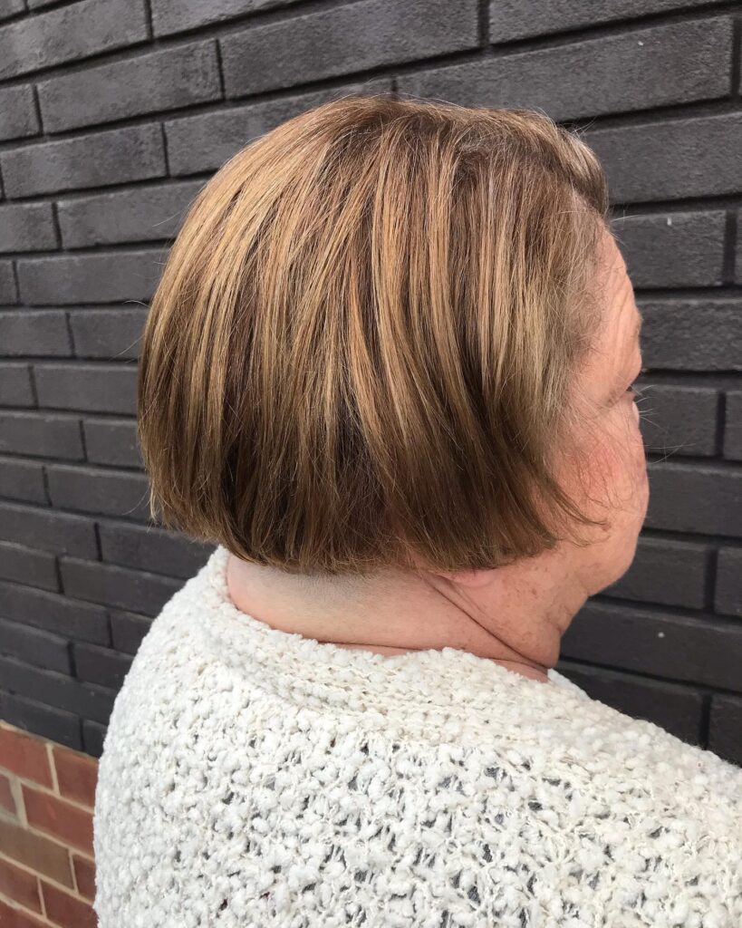 A woman viewed from behind wearing a classic chin-length bob with copper and blonde highlights and a blunt-cut neckline.