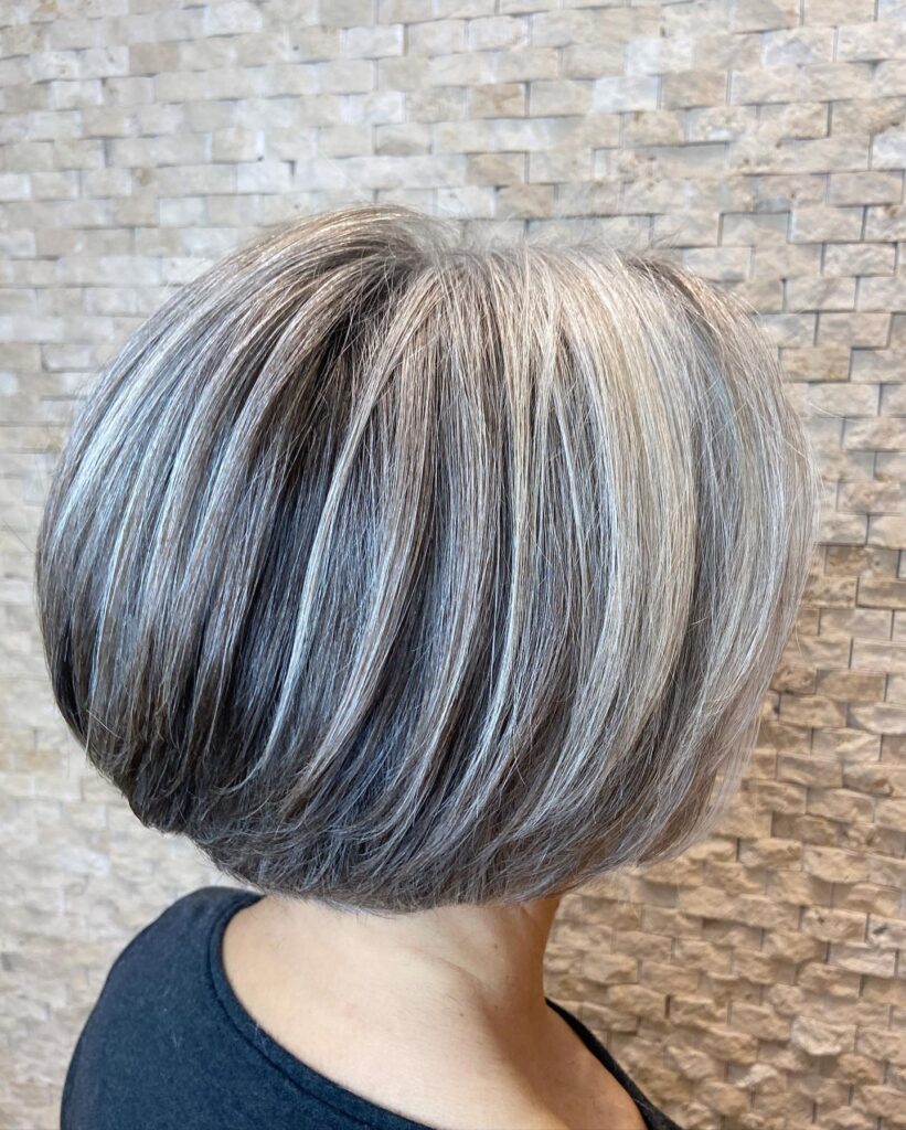 A woman is viewed from the back, showing a rounded layered bob with a mix of dark charcoal and bright silver highlights.