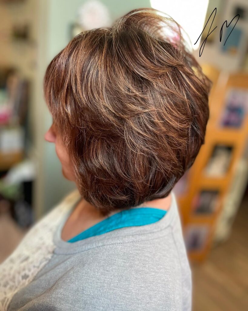 A woman with a neck-length auburn bob featuring copper highlights and voluminous, flicked layers.