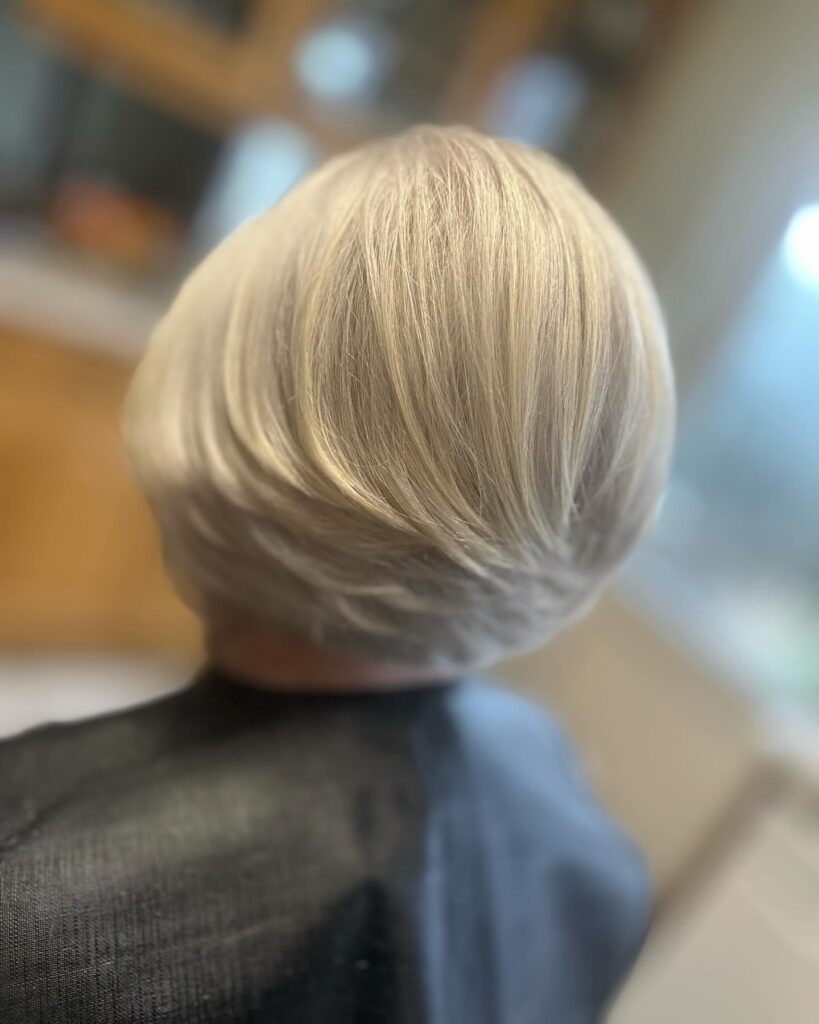 A woman with a rounded platinum blonde bob featuring short tapered layers at the nape and a voluminous crown.