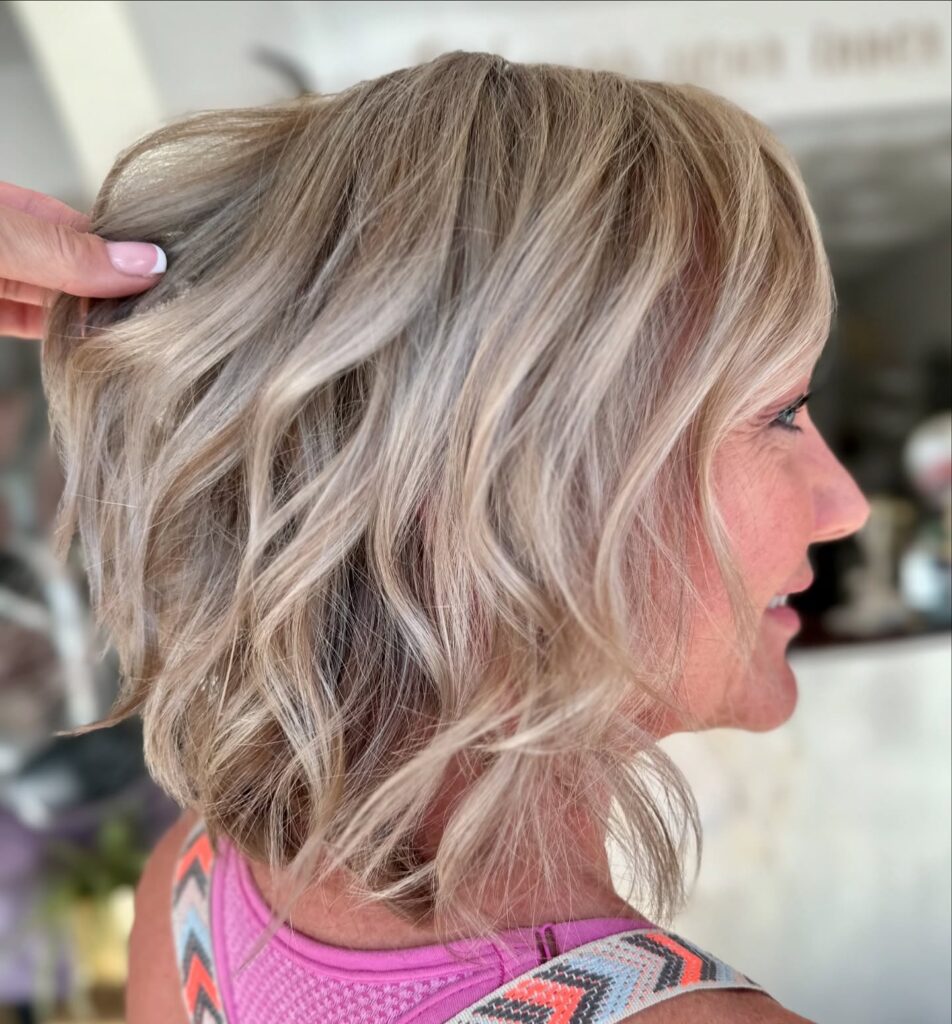 A woman with a neck-length ash blonde bob featuring loose beachy waves and shattered layers.
