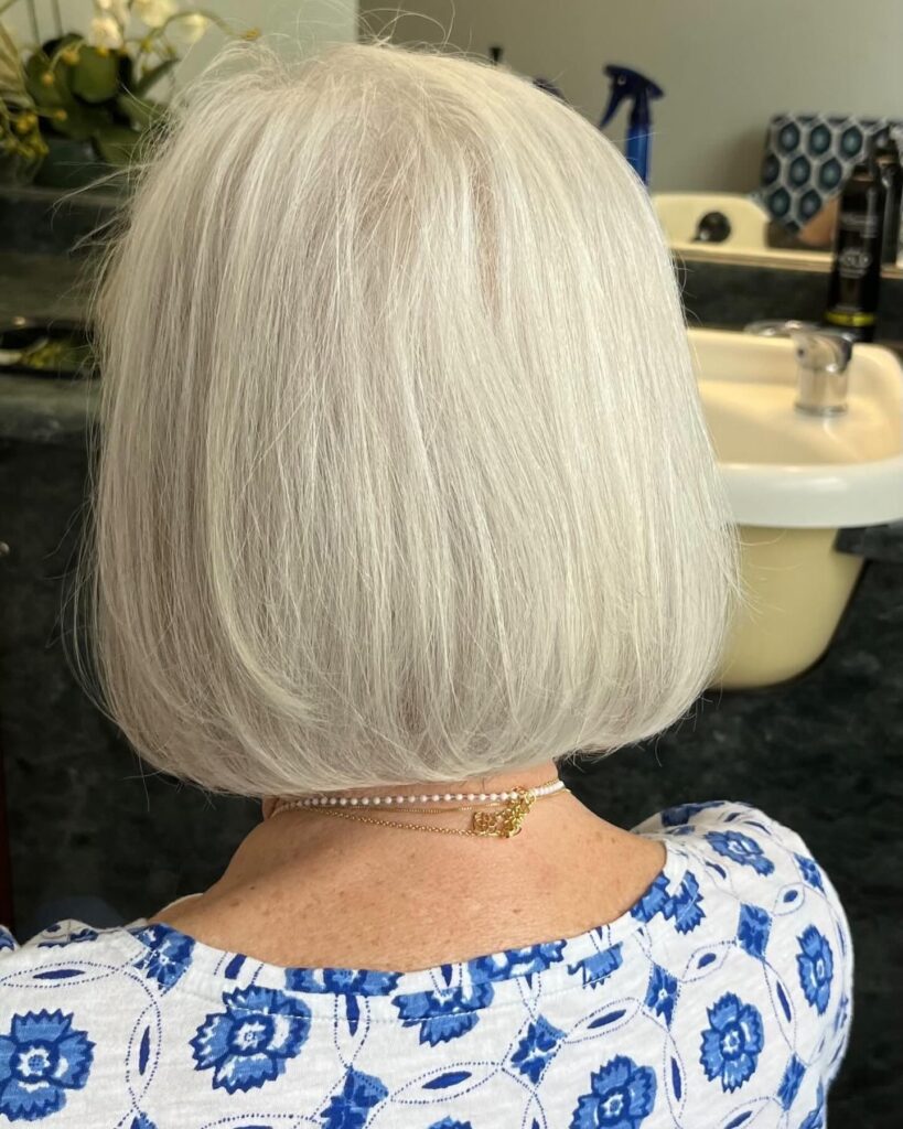 A woman from behind with a chin-length bright silver blunt bob that curves inward at the ends.
