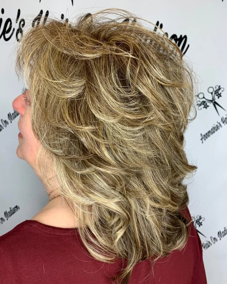 A woman with a medium-length sandy blonde feathered shag haircut featuring high-volume layers and wispy flipped ends.