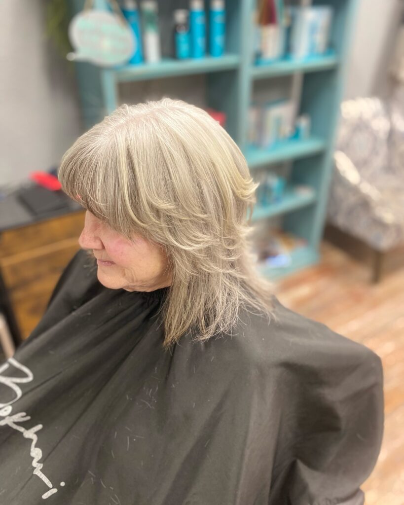 A woman with a medium-length platinum blonde haircut featuring feathered layers and a soft full fringe.