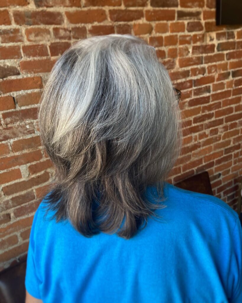 A woman viewed from behind is showing a medium-length silver and gray layered bob with tapered wispy ends.