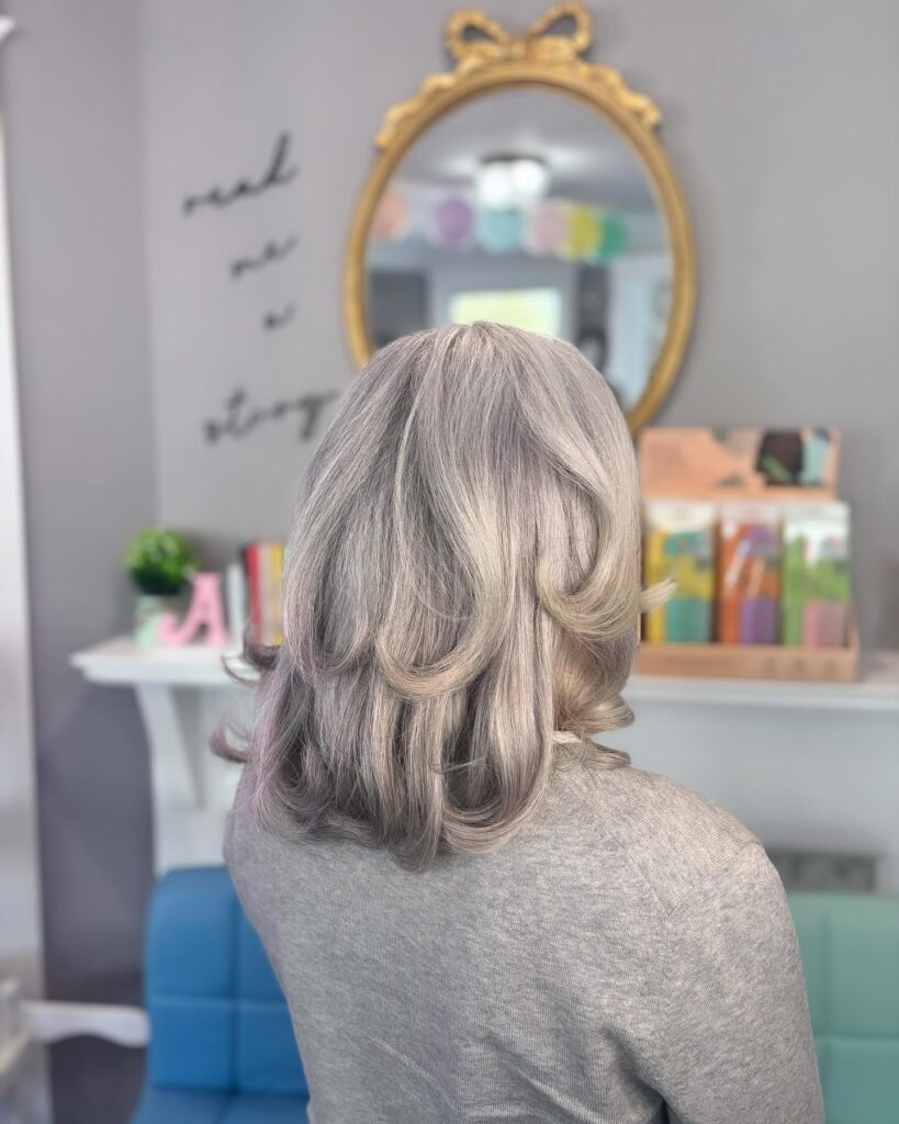 A back view of a woman with medium-length, mushroom-blonde hair featuring soft, voluminous curls and subtle layers.