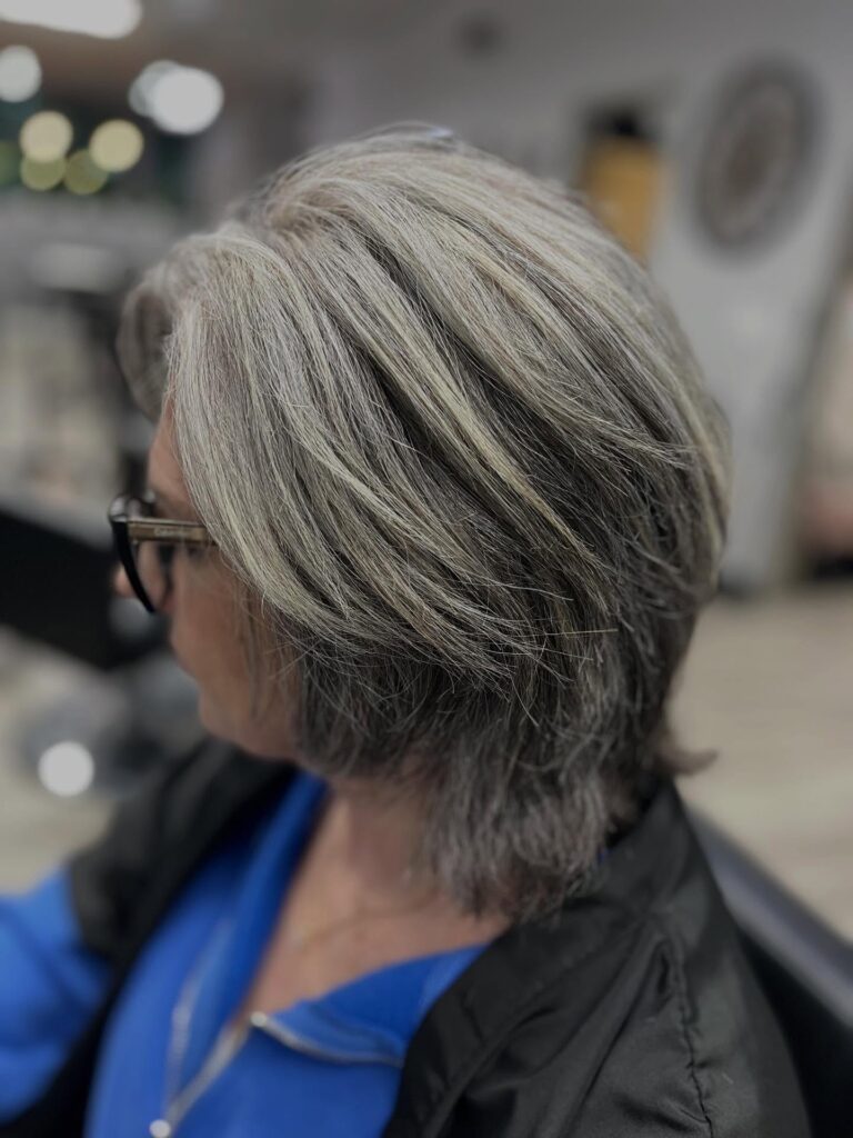 A woman with a medium-length ash gray and silver layered bob featuring textured ends and side-swept styling.