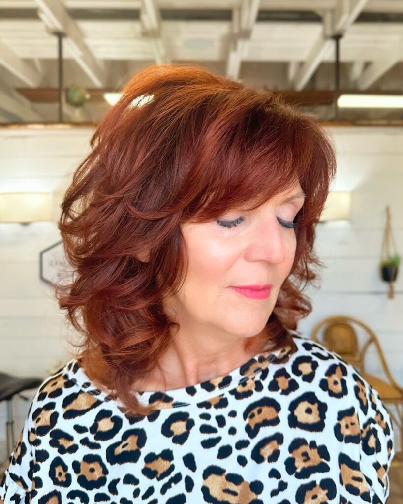 A woman with a medium-length mahogany red shag haircut featuring voluminous chunky layers and side-swept bangs.
